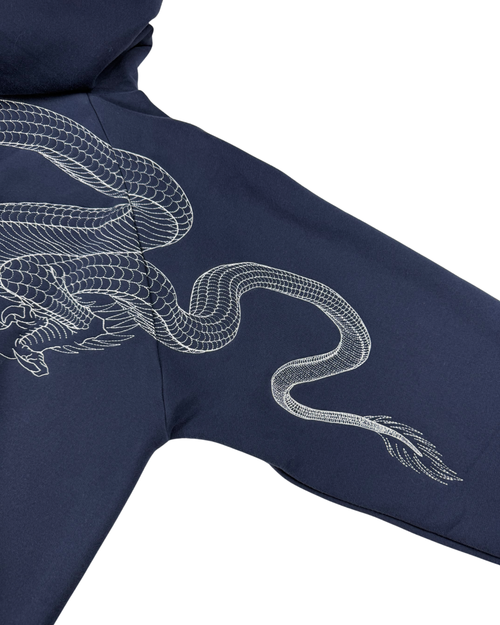 Close-up of a navy blue hoodie sleeve featuring a detailed white embroidered dragon design, shown against a plain white background.
